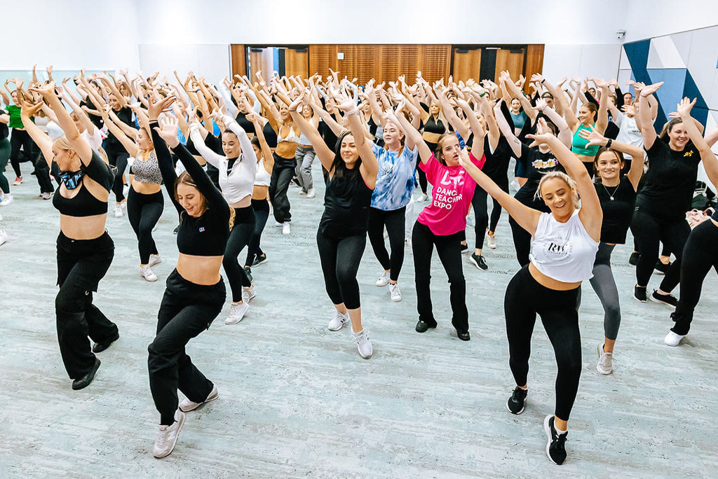 Dancers in a packed movement class with arms raised